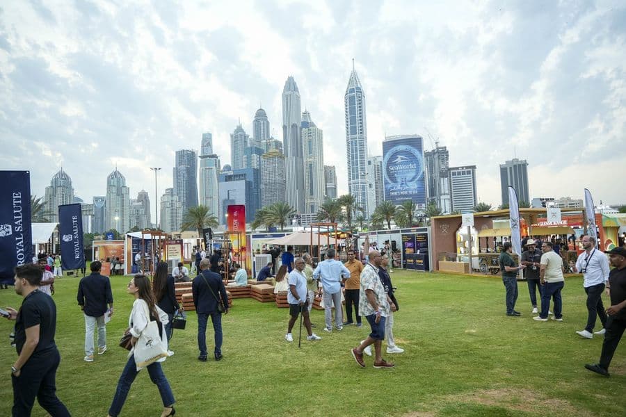 Festival-goers on the lawn at MaltLive Dubai with the Dubai Marina skyline behind the pavilions