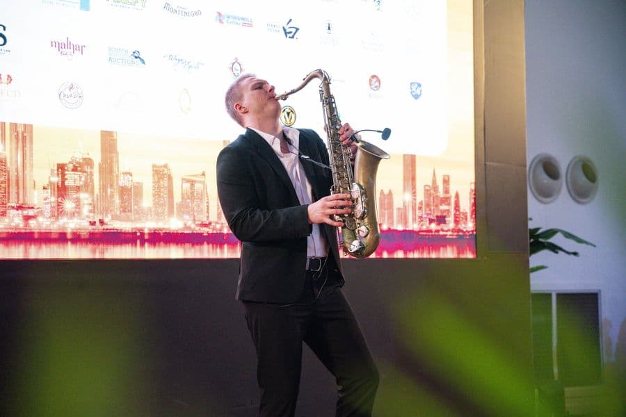A saxophonist playing against a lit skyline backdrop